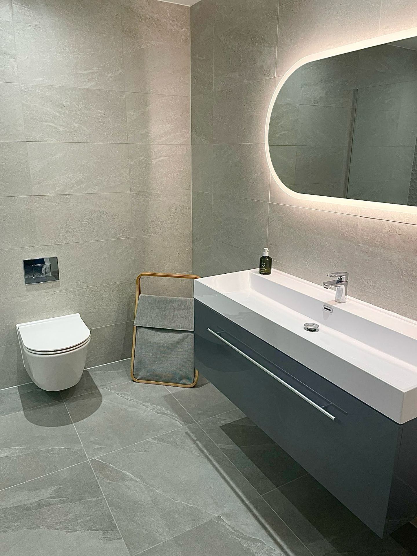 Navy vanity and wall hung toilet in a stone tiled Essex bathroom